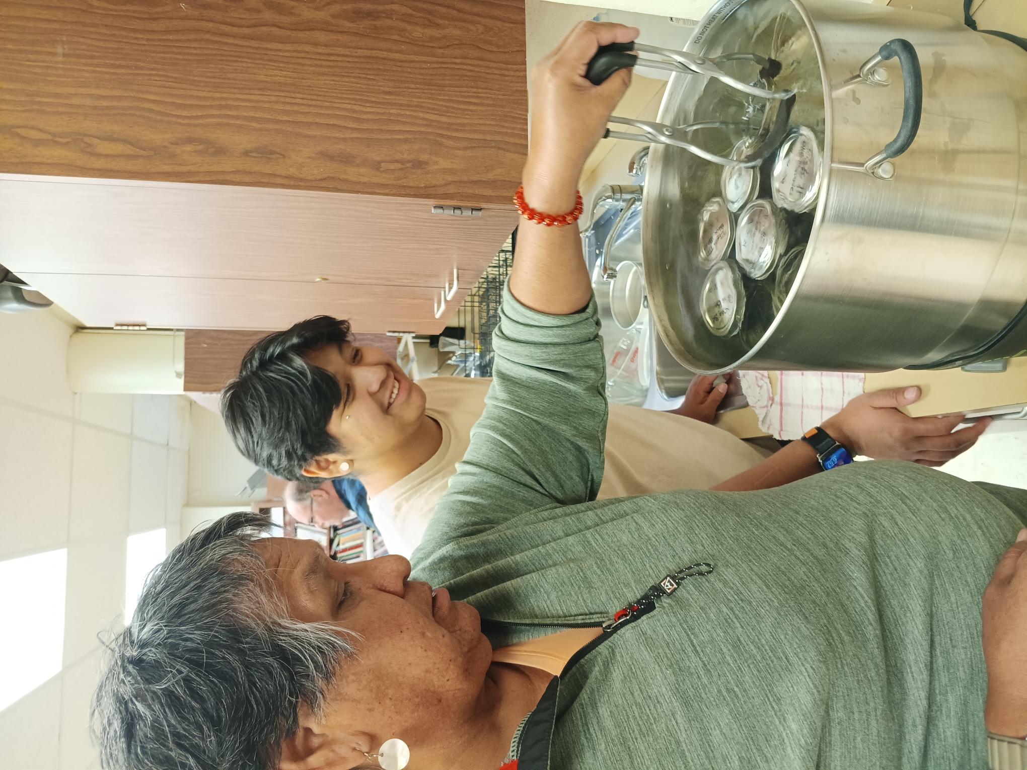 Family teamwork: Mother carefully lowers jars of fresh blueberries into the hot water bath during canning class. 